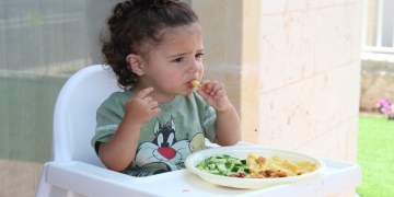 niña comiendo verduras con la mano en su sillita