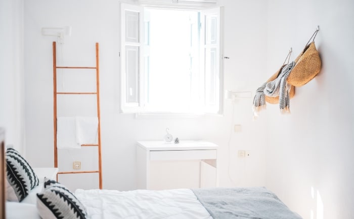dormitorio en blancos, con ventana en blanco y algún detalle decorativo en madera, con cojines oscuros