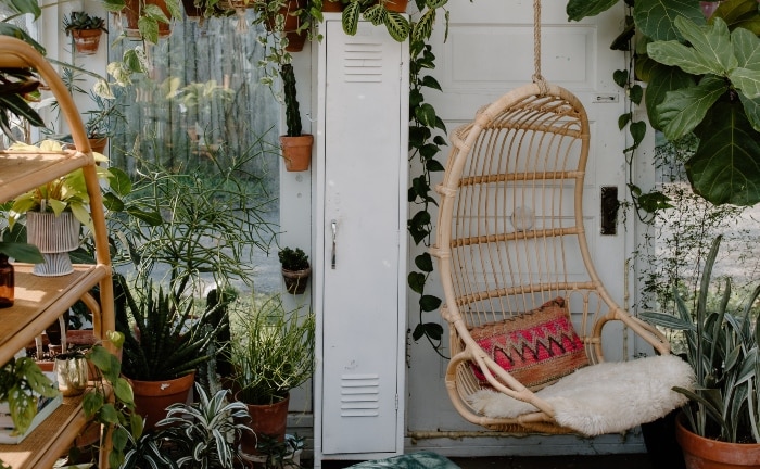 sillón colgante en bambú con cojín rojo y muchas plantas