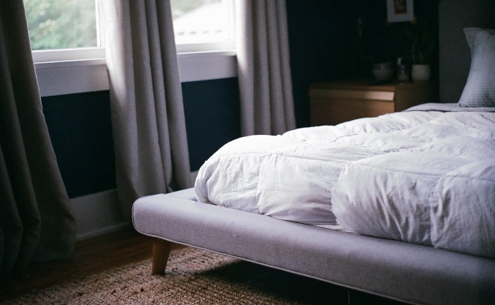 cama con nórdico blanco, somier gris, alfombra y ventana con cortinas