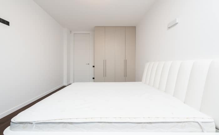 habitación en tonos blancos, sin sábanas, con armario beige al fondo