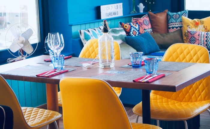 comedor con sillas en amarillo, mesa puesta de ristal y sofá azul con colorido