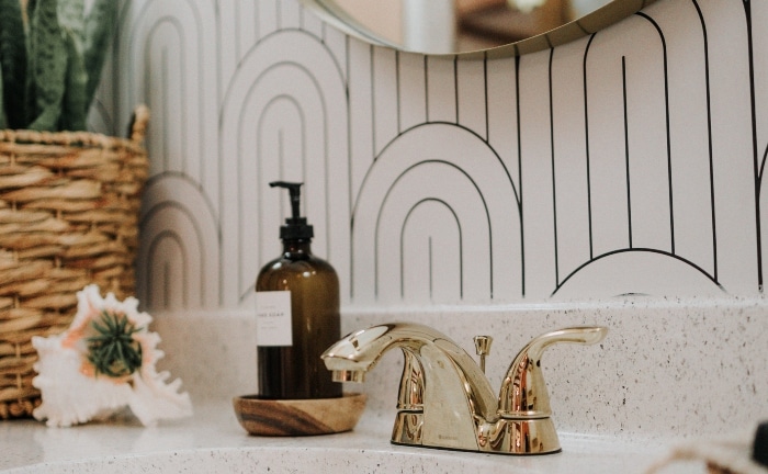 detalle lavabo del baño con grifo dorado y papel pintado en blanco y negro