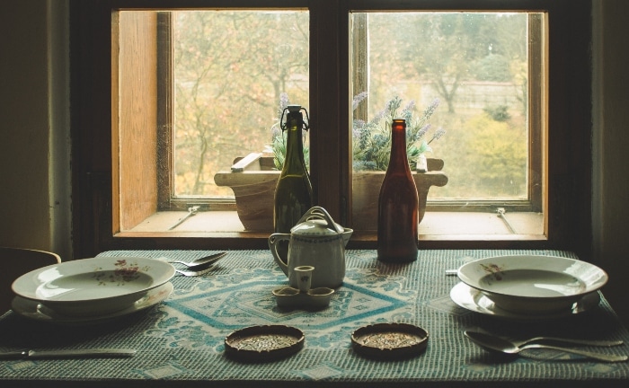 mesa estilo rústico con dos botellas, vajilla retro con flores y ventana