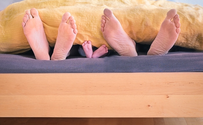 pis de una familia sobresaliendo de cama con somier de madera