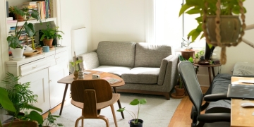 salón con sofá fris, mesa con silla, estantería y diversas plantas