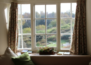 ventana blanca con cortinas de flores, cojines en verde y varios elementos decorativos