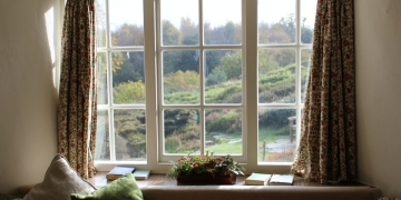 ventana blanca con cortinas de flores, cojines en verde y varios elementos decorativos