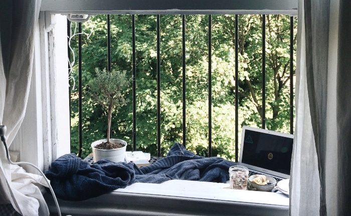ventana con rejas a modo despacho, con planta, vaso con piedras, una manta azul y ordenador