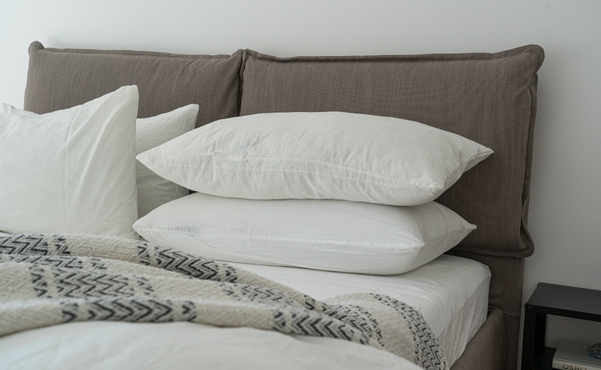 cama con cuatro almohadas con funda blanca, cabecero d etela marrón y manta en tonos crudos