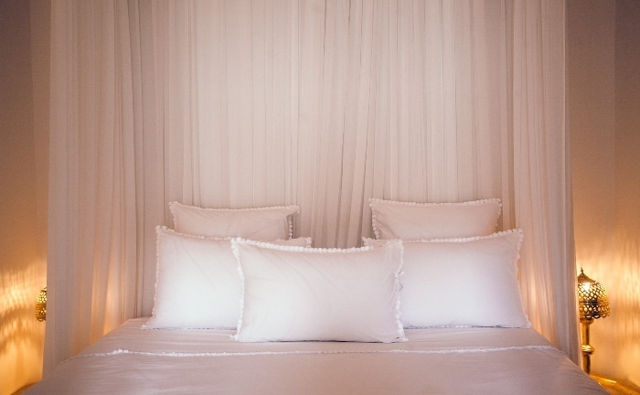 cama con cinco almohada, todo en blanco, en habitación don dosel y dos lámparas iluminando al fondo