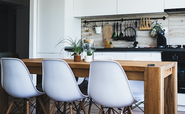 cocina sostenible con mesa de madera y tres sillas blancas. dos plantas en la mesa y muebles cocina en blanco y negro