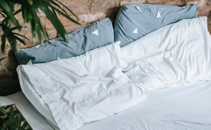 cama en habitación con pared de piedra, sabanas y dos almohadas con fundas blancas y otras dos azules con triángulos blancos