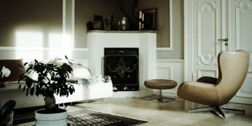 salón con chimenea en tonos beige, cuenta con mesa con planta y mesa auxiiar junto a la butaca