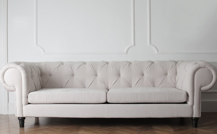 sofá chester en blanco roto ante pared blanca y suelo de madera