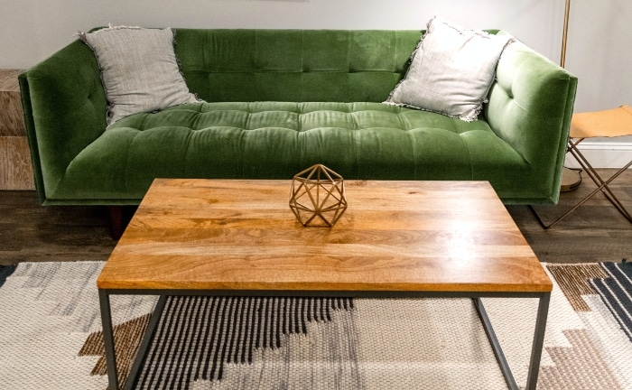 sofá verde con dos cojines crudos, en salón con mesa central de madera y hierro, con figura en cima y alfombra en crudos